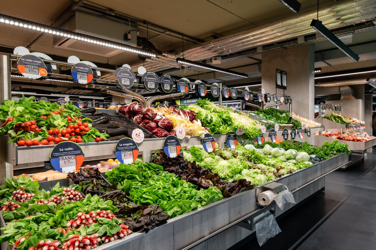 Vue d'un rayon de légumes frais dans un supermarché, éclairé par des luminaires modernes.