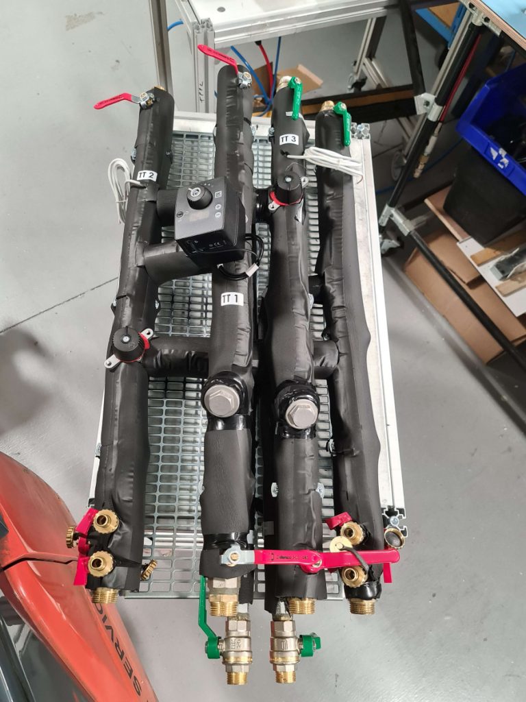 Photo d’un module hydraulique assemblé avec tuyauteries isolées en mousse noire, électrovanne et raccords en laiton, installé dans un châssis métallique.