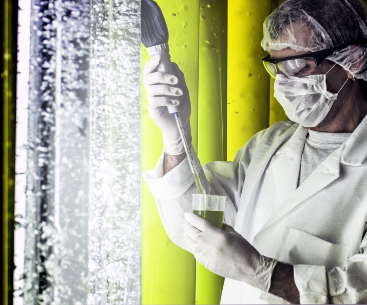 Technicien de laboratoire en blouse blanche manipulant une solution verte à l’aide de matériel scientifique.