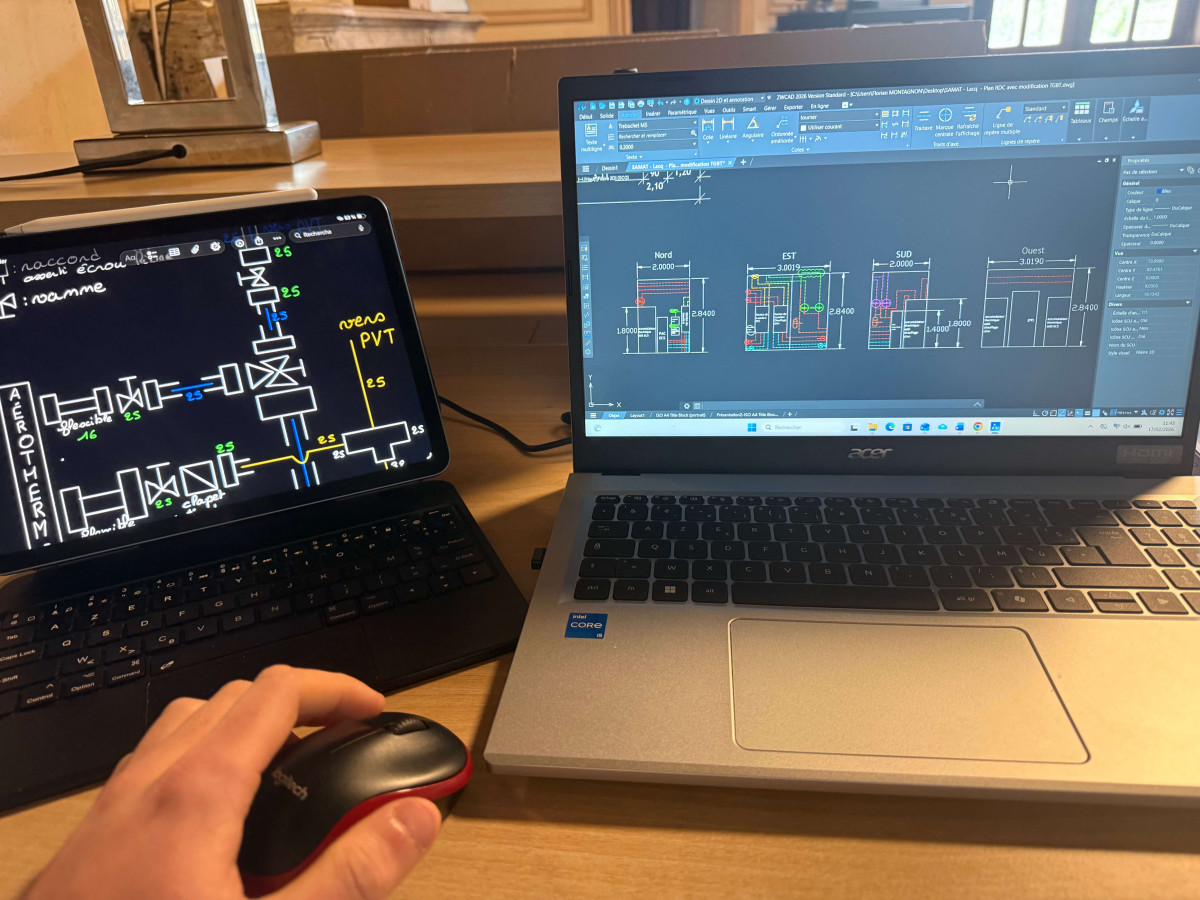 Poste de travail en bureau d’études avec ordinateur portable et écrans affichant des plans sur un logiciel. 