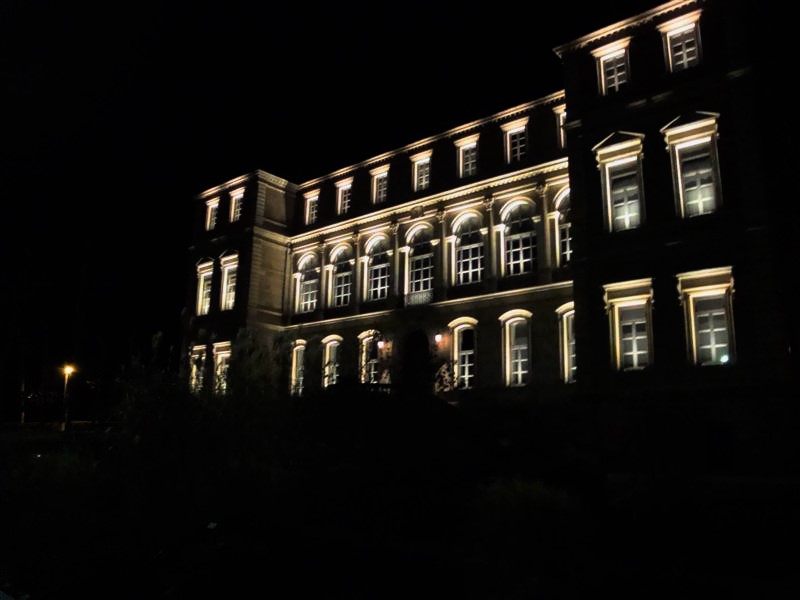 Façade d’un bâtiment éclairée la nuit, avec de grandes fenêtres et une illumination chaleureuse mettant en valeur l’architecture.