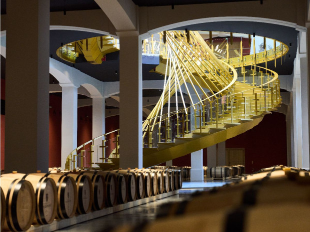 Grand escalier en colimaçon aux caractéristiques architecturales, couleur doré avec des rampes en verre, visible à l'intérieur d'un bâtiments.