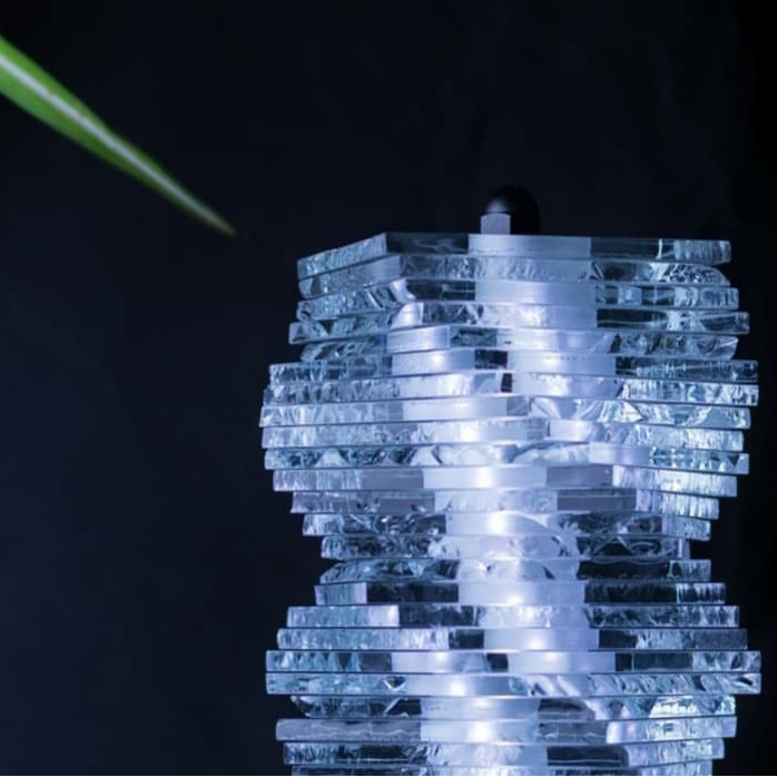 Détail d’un luminaire constitué de plaques de verre superposées autour d’une source lumineuse centrale blanche, créant un effet de transparence et de relief.