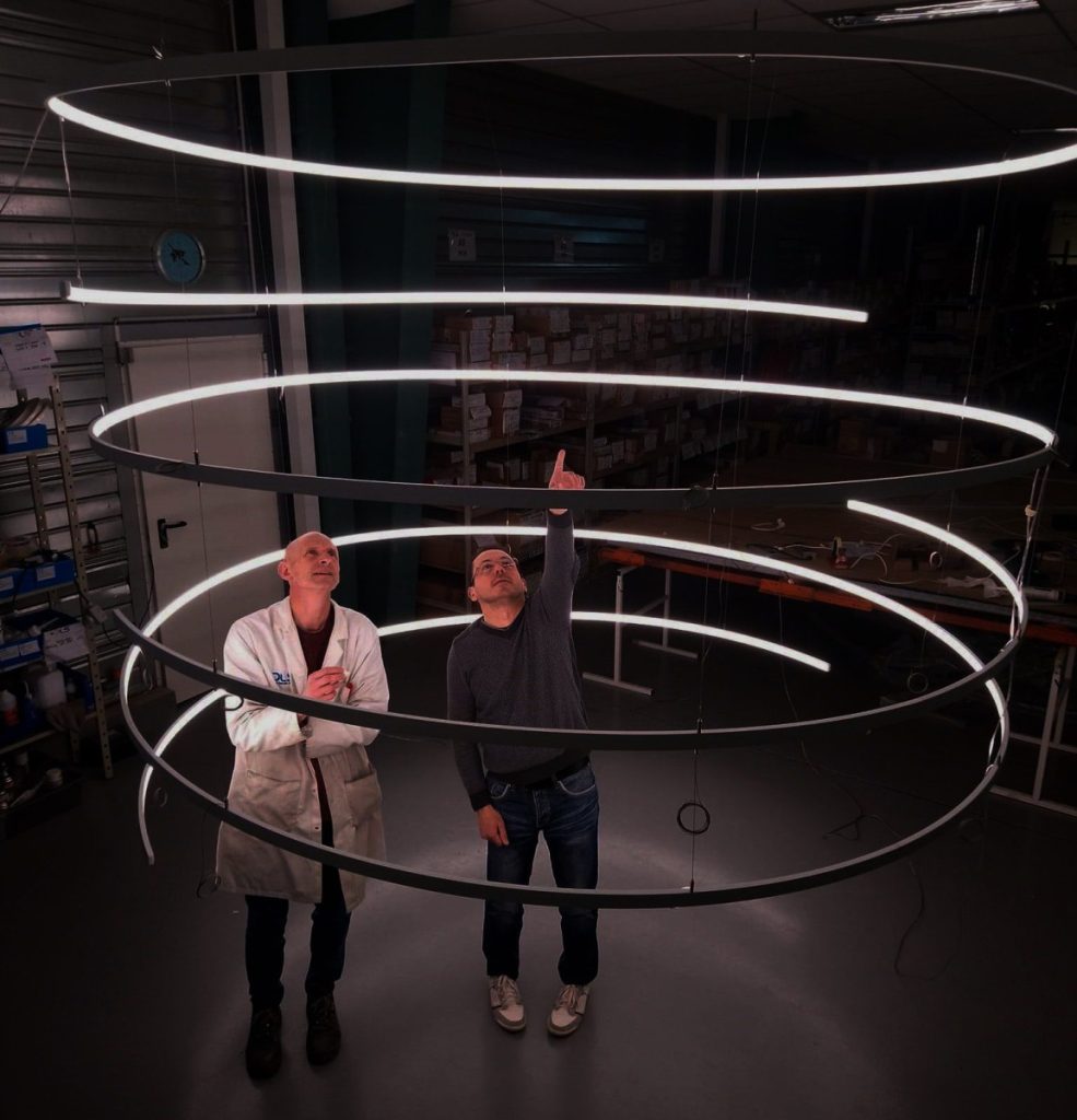 Deux techniciens inspectent un plafonnier en spirale, l’un d’eux pointant un élément du luminaire.