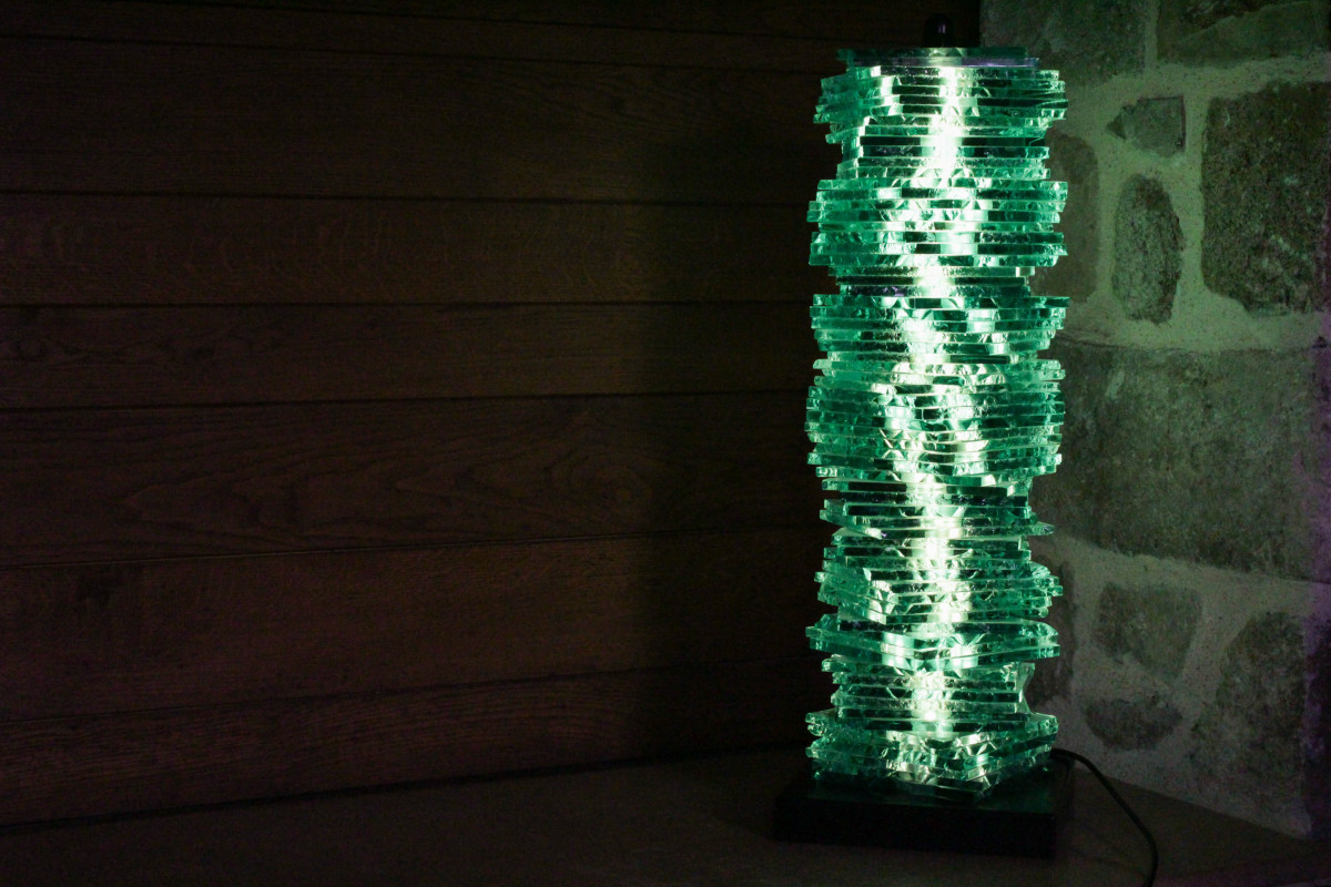 Colonne lumineuse composée de multiples couches de verre superposées, diffusant une lumière verte dans un espace sombre.