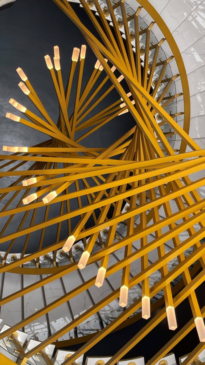 Zomm sur les luminaire d'un grand escalier en colimaçon aux caractéristiques architecturales, couleur doré avec des rampes en verre, visible à l'intérieur d'un bâtiments. 